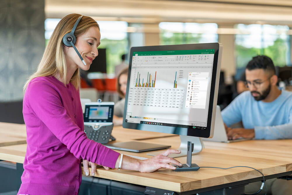 Eine Frau bedient an ihrem Arbeitsplatz das Cisco Headset über die Multibasestation