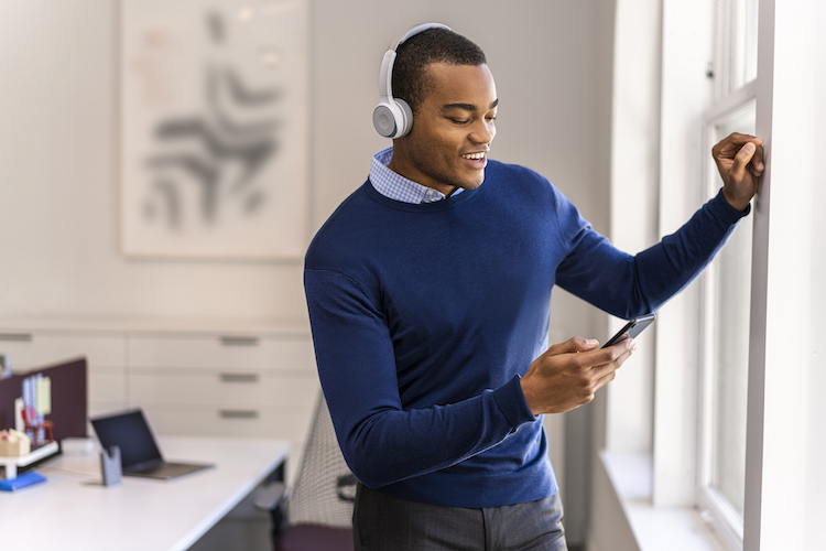 Ein Mann lehnt sich an das Fenster seines Homeoffice, während er über das Cisco 730 Headset telefoniert