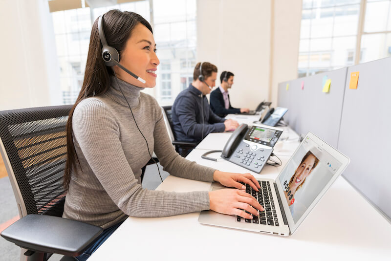 EIne Frau telefoniert im Büro über das Headset und ihr IP-Telefon, während sie den Computer nutzt