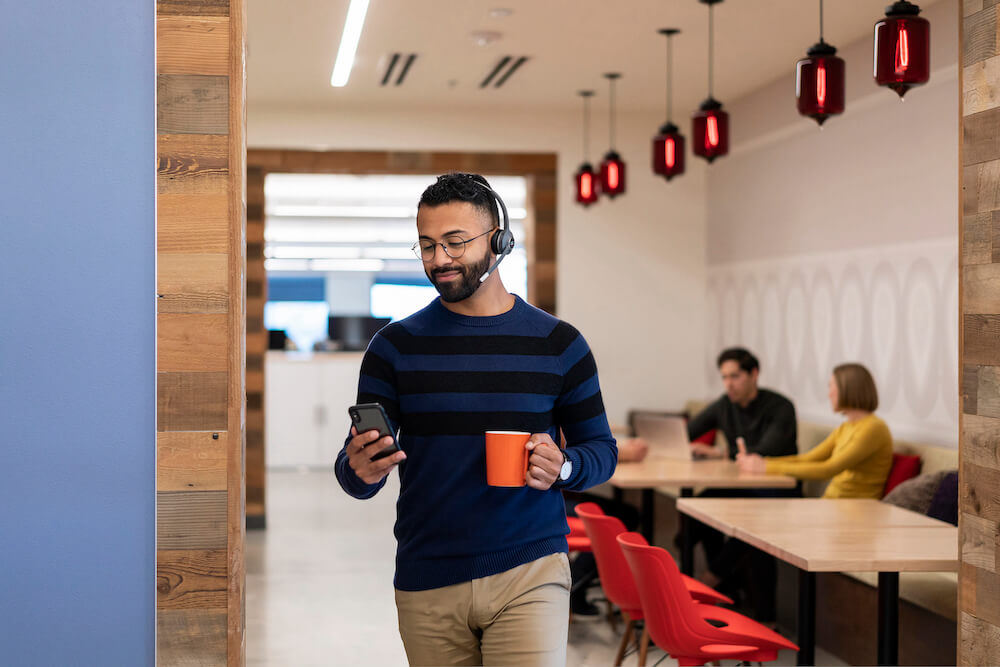 EIn Mann telefoniert mobil über das Headset, während er durch das Büro läuft